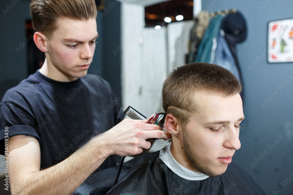 Fototapeta premium Great time at barbershop. Cheerful young bearded man getting haircut by hairdresser while sitting in chair at barbershop