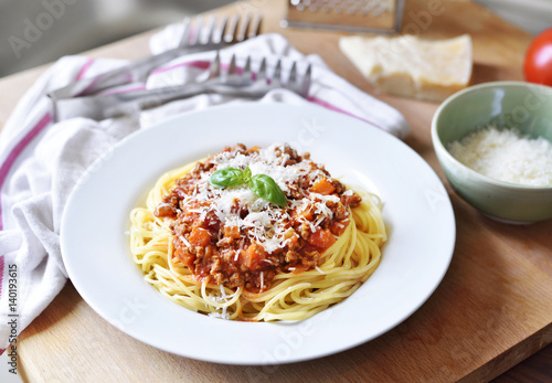 Spaghetti Bolognese on a white plate with decorative basil leaf. Italian cuisine, pasta with tomato sauce and parmesan cheese.
