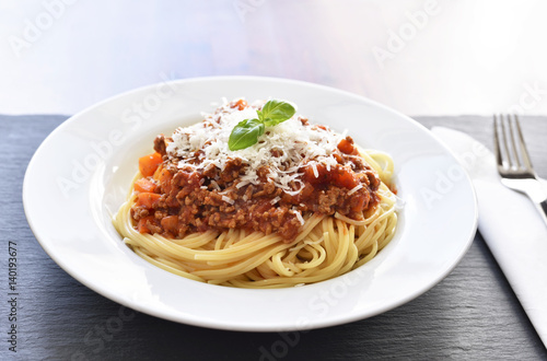 Spaghetti Bolognese on a white plate with decorative basil leaf. Italian cuisine, pasta with tomato sauce and parmesan cheese.