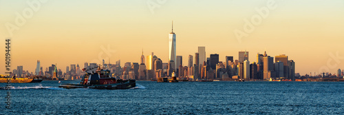 Panoramic Sunset of Lower Manhattan and New York City Harbor with Financial District skyscrapers and passing tugboat