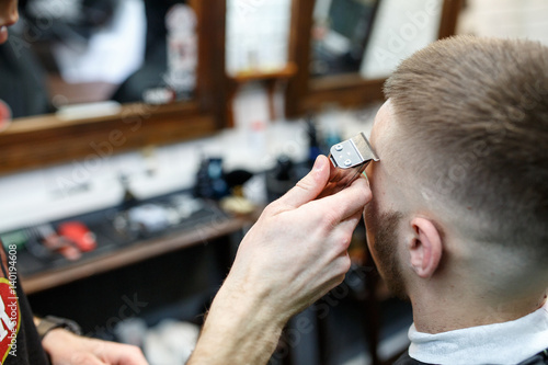 Great time at barbershop. Cheerful young bearded man getting haircut by hairdresser while sitting in chair at barbershop