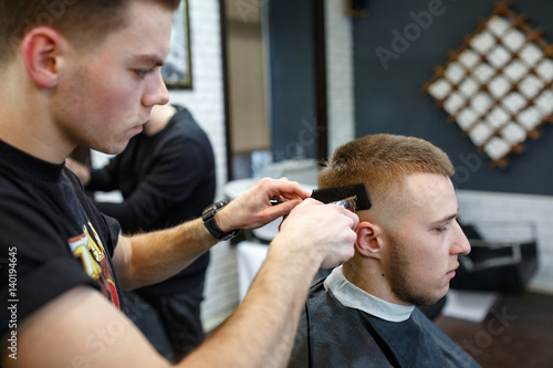 Great time at barbershop. Cheerful young bearded man getting haircut by hairdresser while sitting in chair at barbershop