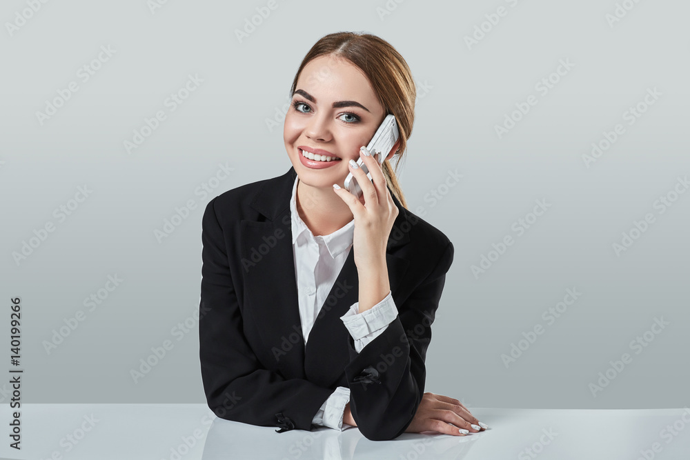 attractive dark-haired woman dressed in a black suit is sitting at table in an office. attractive dark-haired woman dressed in a black suit is sitting at table in an office.