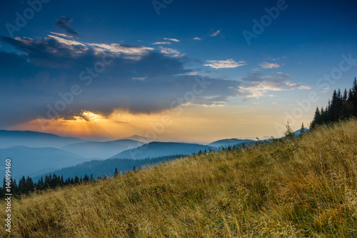 Sunrise above peaks of smoky mountain with the view of forest in the foreground. Dramatic overcast sky. 