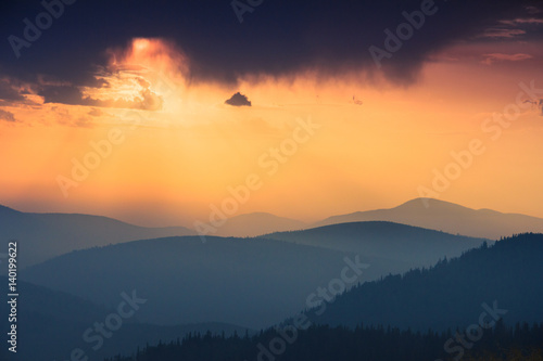 Fantastic sunrise above peaks of smoky mountain with the view into misty hills. Dramatic overcast sky. Mountains silhouettes.