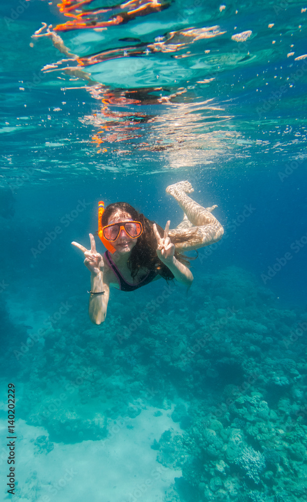 Girl in swimming mask dive underwater near coral reef 