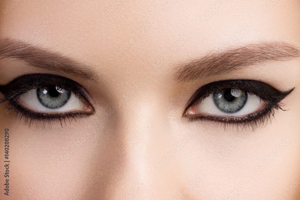 Naklejka premium Piękna kobieta z jasny makijaż oczu z seksownym czarnym makijażem liniowej. Fason duży kształt strzałki na powiece kobiety. Elegancki makijaż wieczorowy