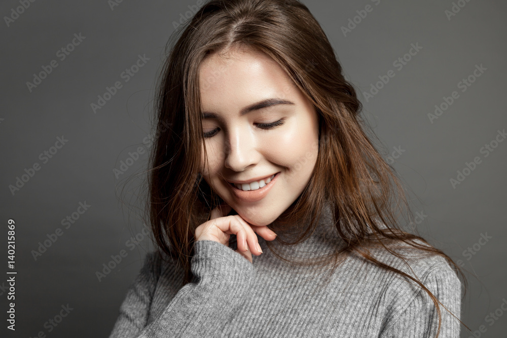 Happy smiling young model woman with clear skin looking at the camera on gray background Happy smiling young model woman with clear skin looking at the camera on gray background