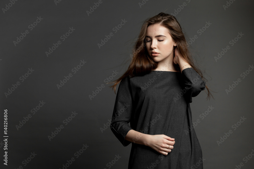 Cute boring brunette model girl in dark dress on gray background. Cute boring brunette model girl in dark dress on gray background.