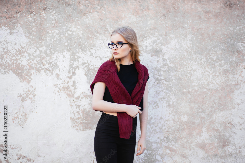 Portrait of a young girl with glasses and professional make up standing near a wall Portrait of a young girl with glasses and professional make up standing near a wall
