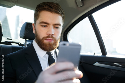 Concentated bearded business man in suit looking at mobile phone in his hand © Drobot Dean