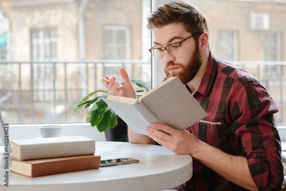 Serious young man reading books while using laptop Serious young man reading books while using laptop