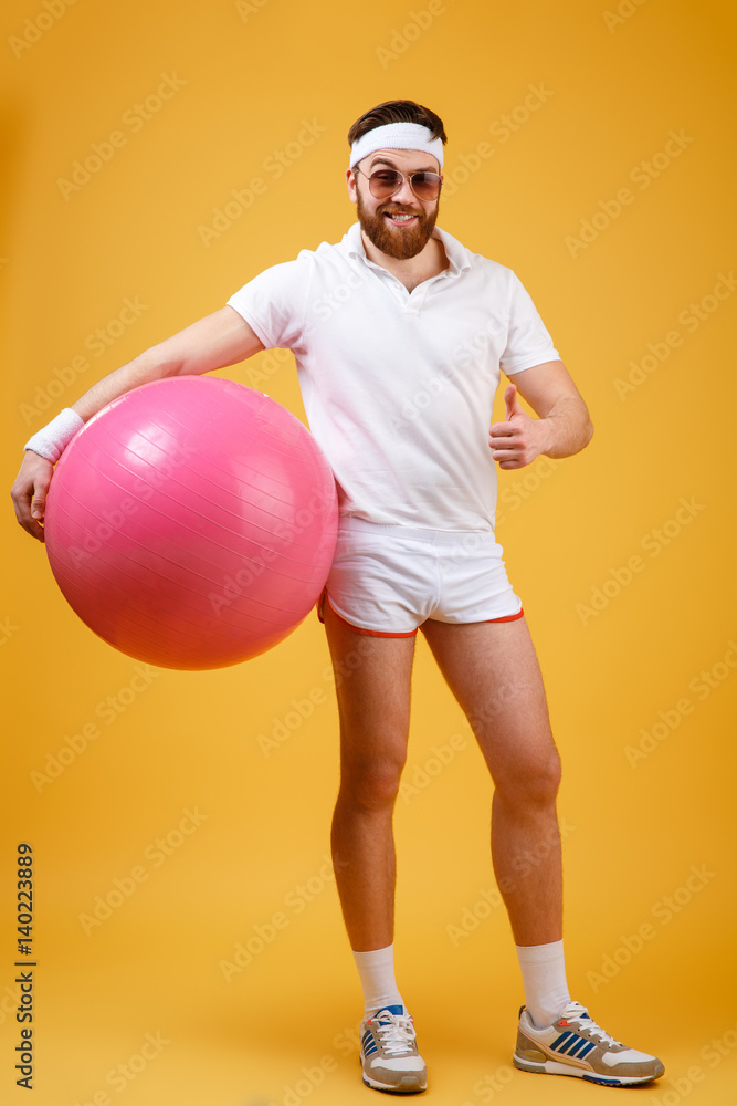 Vertical image of sportsman holding fitness ball showing thumb up Vertical image of sportsman holding fitness ball showing thumb up