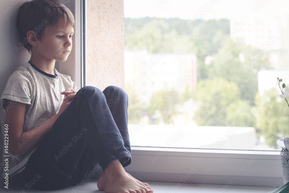 Sad child sitting on window shield and looking out the window
