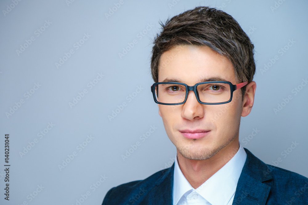 Close up Smiling Young Businessman Wearing Eyeglasses, Looking at the Camera Against Gray Wall Background