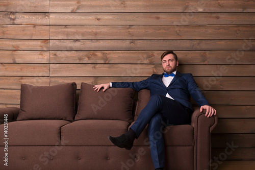 Serious groom in suit and bow-tie sitting on couch © Nomad_Soul