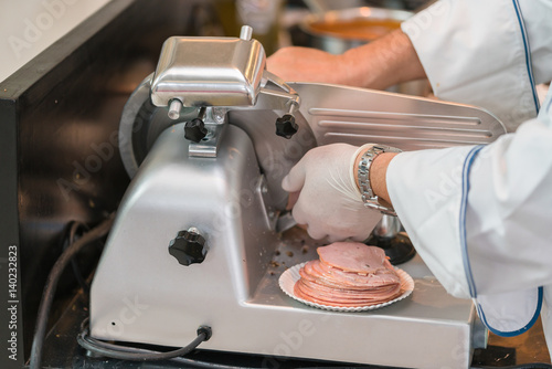 chef wearing rubber glove  using ham slicer machine photo