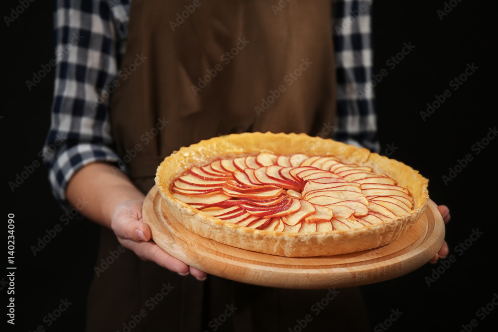 Φωτογραφία Woman holding wooden tray with apple pie on dark background
