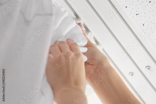 Woman hanging curtains over window, closeup