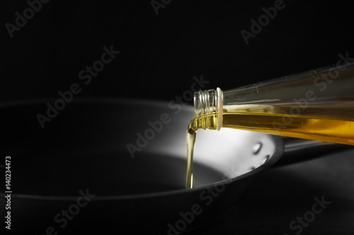 Pouring oil from bottle into pan on dark background