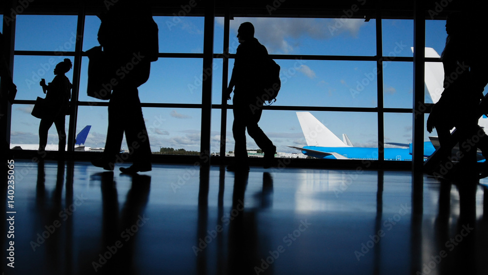 Travellers with suitcases and baggage in airport walking to departures in front of window, silhouette