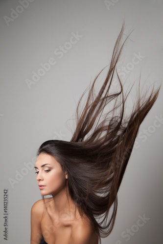 Young woman posing with her long hair thrown up. Vertical studio shot.