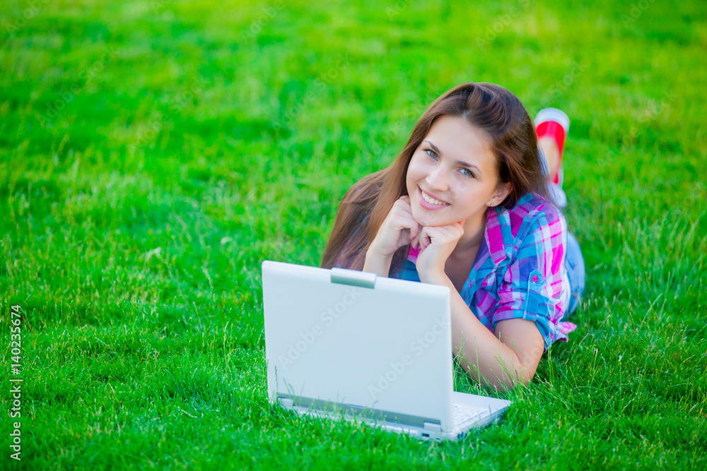 beautiful young girl lying on the field with laptop on the wonderful grass background beautiful young girl lying on the field with laptop on the wonderful grass background