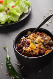 Kidney Bean Chili with tomato chunks and onion topped with cheese in large black bowl on dark charcoal background