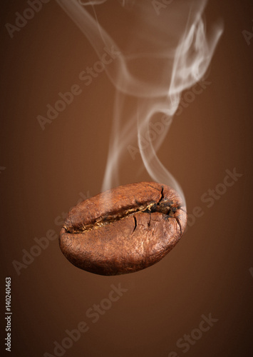 Closeup falling coffee bean with smoke on brown background photo