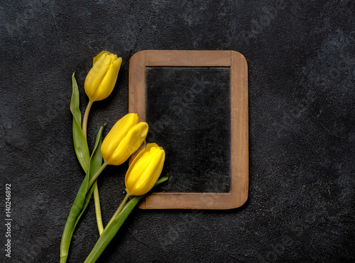 Yellow tulips on dark background with antique halk wooden board. photo