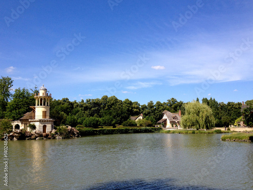 The Hameau de la Reine  The Queens Hamlet  built by Richard Mique for Marie Antoinette at the Chateau de Versailles near Paris  France. Marlborough Tower and cottage by the water s edge on sunny day.