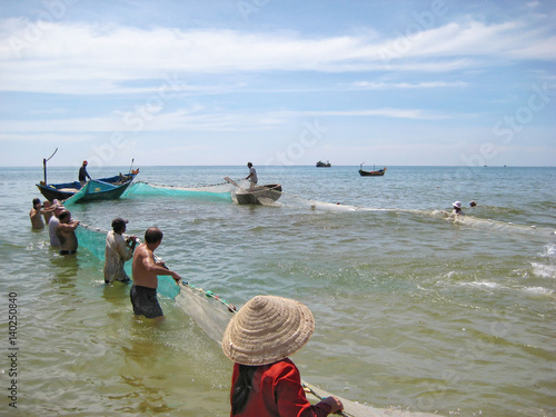 Native fishermen drag fishing net with fish catch out from the ocean on Mui Ne Beach, Vietnam photo