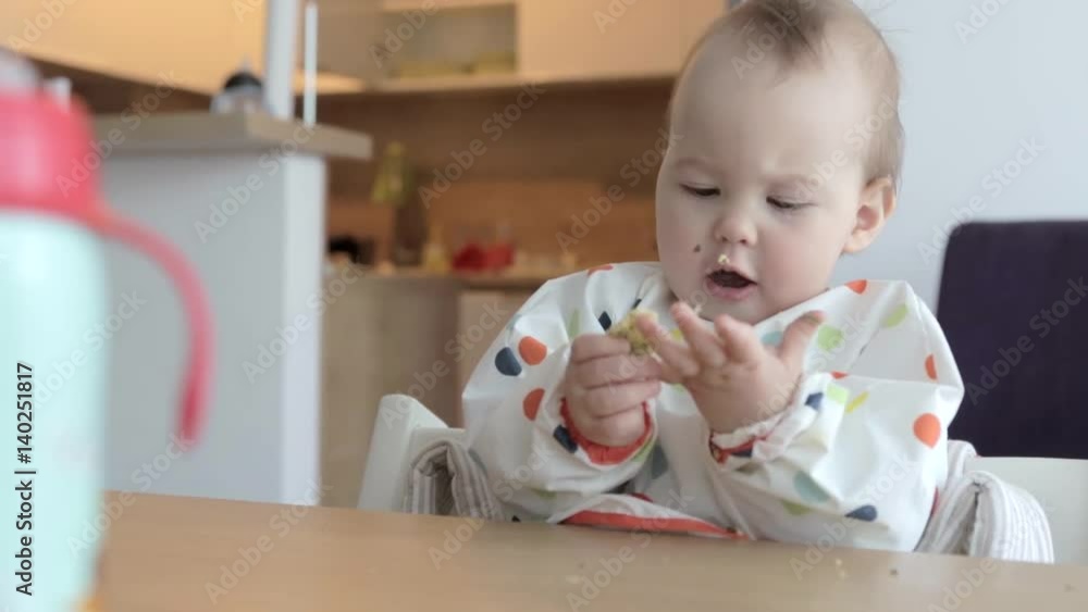 Eleven months old baby girl sitting by the desk, eating food with her fingers; baby led weaning; concept of family life and parenting Eleven months old baby girl sitting by the desk, eating food with her fingers; baby led weaning; concept of family life and parenting