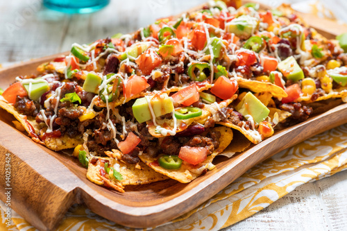 Fotografie Nacho corn tortilla chips with cheese, meat, guacamole and red hot spicy salsa