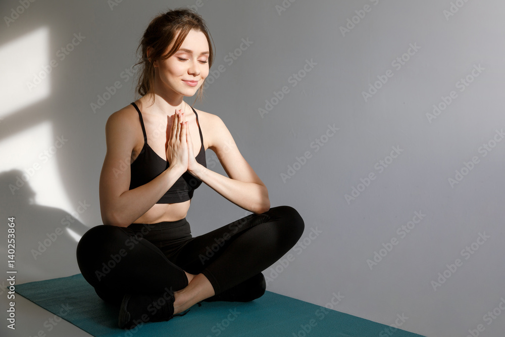 Fototapeta premium Attractive young woman meditating while sitting in lotus pose