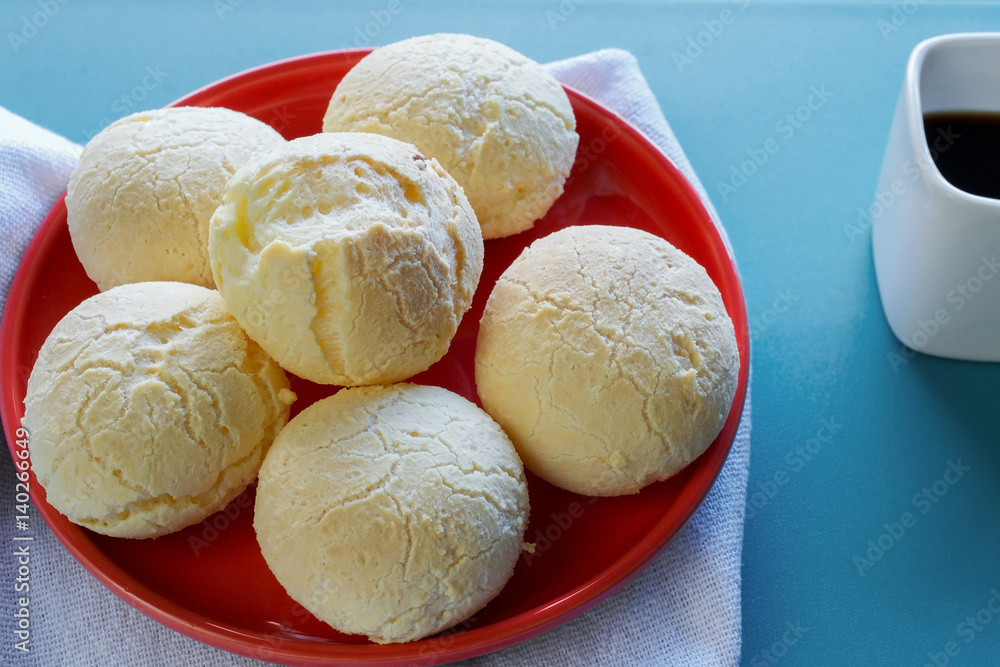 Closeup on mouth-watering Brazilian cheese bread (Pao de queijo) on red plate, on blue wooden table, served with a square cup of espresso coffee Closeup on mouth-watering Brazilian cheese bread (Pao de queijo) on red plate, on blue wooden table, served with a square cup of espresso coffee