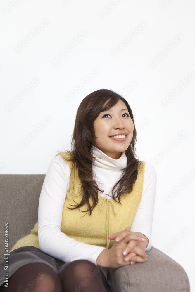 Young woman sitting on sofa, smiling and looking away, white background Young woman sitting on sofa, smiling and looking away, white background