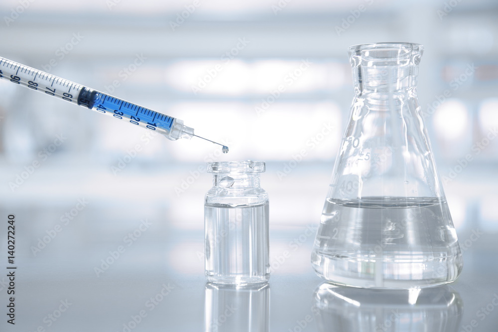 syringe with blue solution with vial and flask in science laboratory