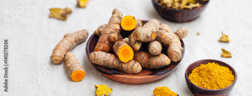 Fresh and dried turmeric roots in a wooden bowl.