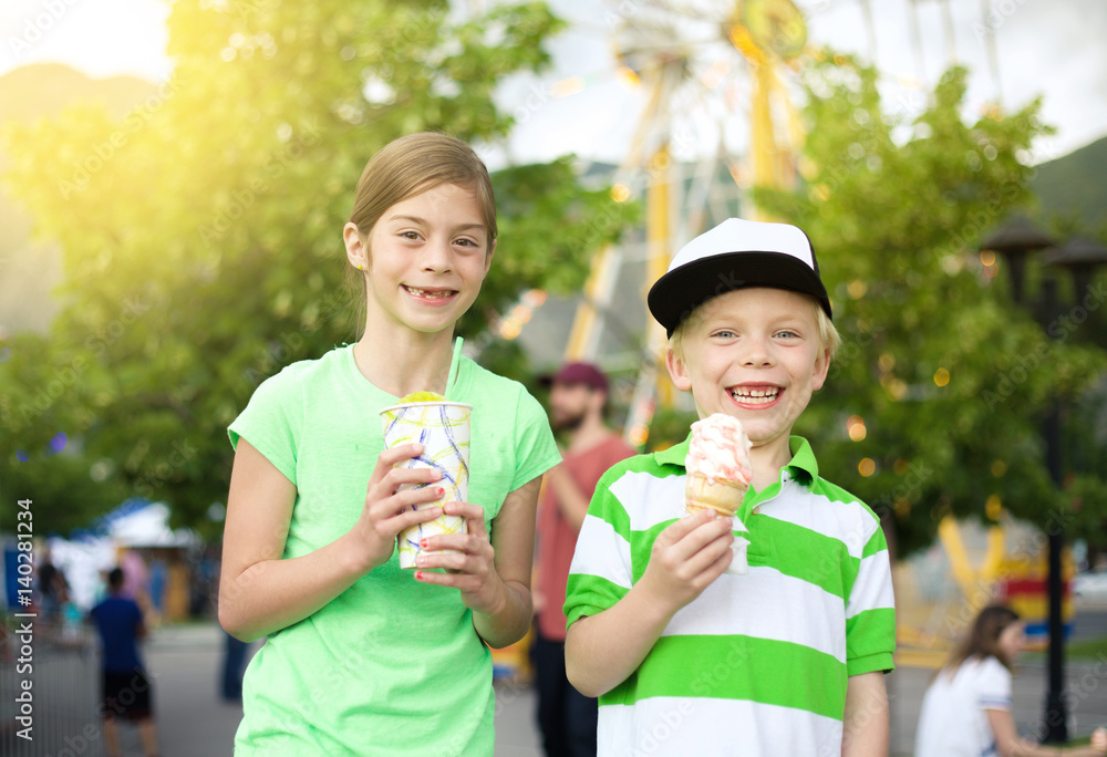 Kids eating ice cream and treats at the carnival. Little boy and girl holding their sweet treat and showing a cheerful smile. Fun summertime activity Kids eating ice cream and treats at the carnival. Little boy and girl holding their sweet treat and showing a cheerful smile. Fun summertime activity