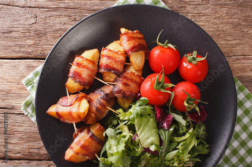 Fried potatoes wrapped in bacon and fresh salad close-up. horizontal top view