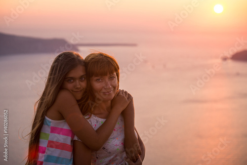 Mother and daughter at sunset. Sunset on the island of Santorini.  Girl tourist on a background of the sea and the setting sun. Mother and daughter travel  