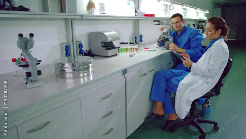 Scientist team working in research lab. Laboratory technicians using tablet pc in lab. Laboratory team working with laboratory tablet. Group of scientists talking with tablet in hands Scientist team working in research lab. Laboratory technicians using tablet pc in lab. Laboratory team working with laboratory tablet. Group of scientists talking with tablet in hands