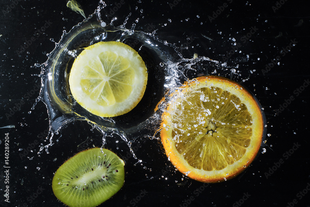 Citrus in water on a black background. Splashing water droplets. Kiwi, lemon and orange Citrus in water on a black background. Splashing water droplets. Kiwi, lemon and orange