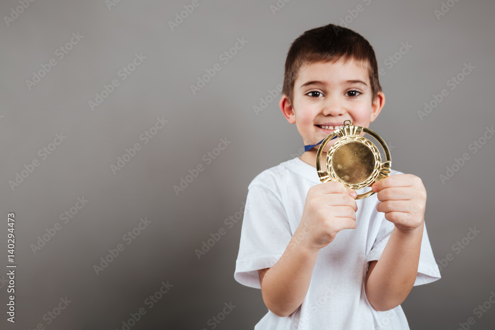 Cheerful little boy showing gold trophy medal
