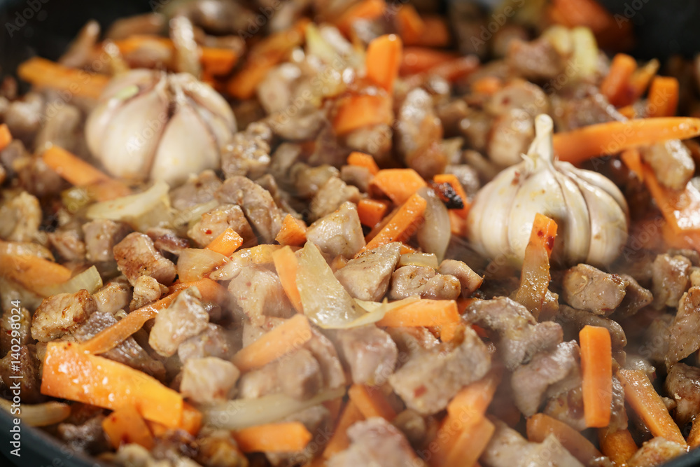 frying pork meat with carrot, onion and garlick for pilaf, closeup macro