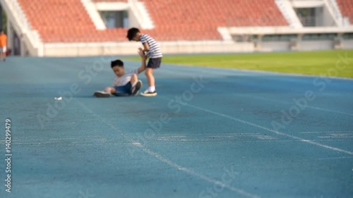 Young Asian boy running on blue track and fall then another boy help him