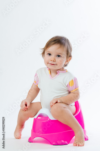 Little smiling girl sitting on a pot. Isolated on white background.