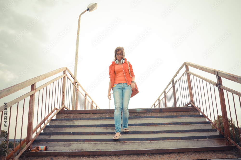 Portrait of a girl going down the stairs, fashion clothes, stylish glasses and headphones.