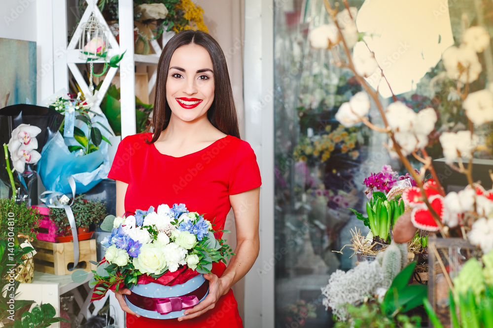 Beautiful brunette in red dress buys a bouquet of flowers in a flower shop